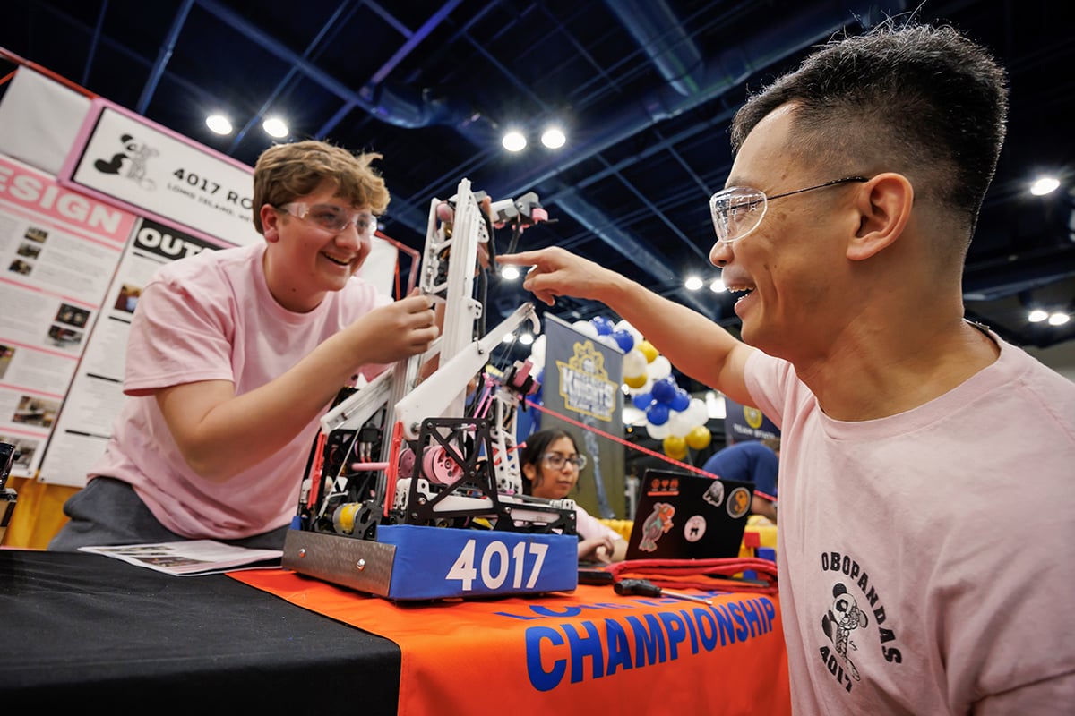 Two FIRST Tech Challenge students working on their robot at FIRST Championship with the help of a FIRST mentor.